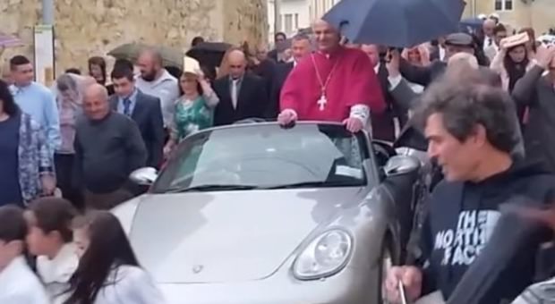 Processione choc: arcivescovo saluta la folla dalla Porsche decappottabile trainata da bambini