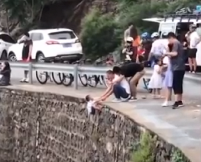 Follia per qualche like in più. Lascia il figlioletto sospeso nel vuoto per una foto: immagini virali – VIDEO