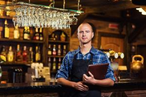 Barman at work in pub,Portrait of cheerful barman worker standing,Waiter giving menus,A pub.Bar.Restaurant.Classic.Evening.European restaurant.European bar.American restaurant.American bar.